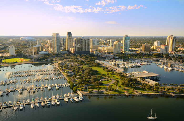 A scenic view of Downtown St. Petersburg, FL, showcasing modern high-rise condos, waterfront views, and vibrant city life under a clear blue sky.